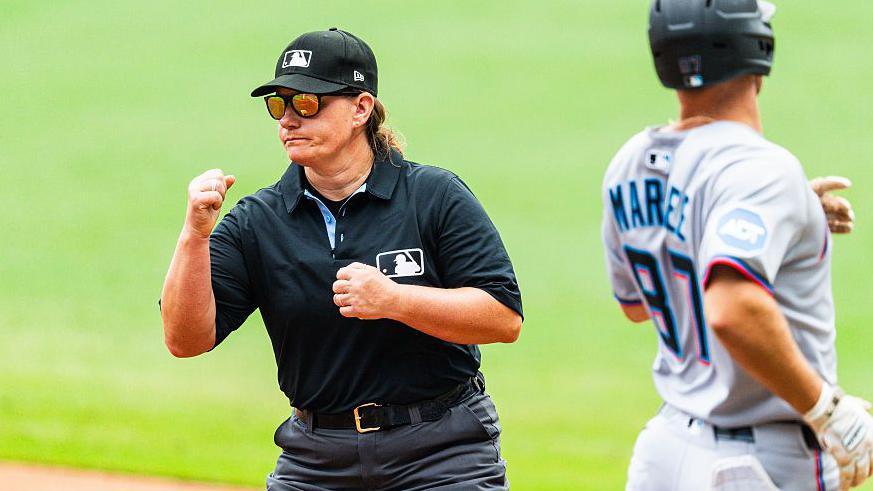 An umpire wearing black does a hand signal to say that the baseball runner is out. 