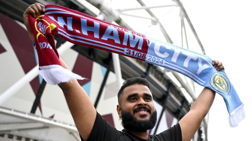 A fan holding up a half-and-half scarf before West Ham's game with Manchester City in August 2024