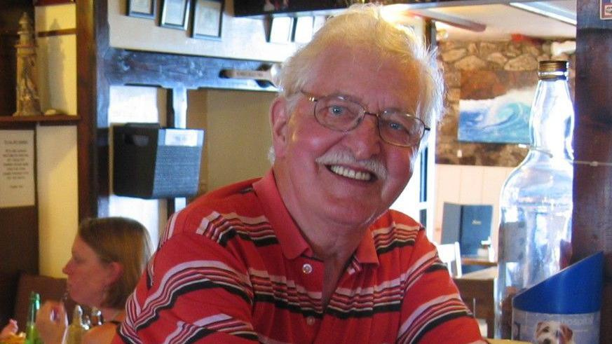 An older man in a red striped polo shirt in a bar