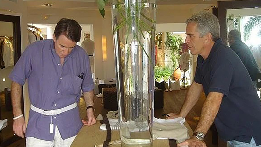 2006 Peter Mandelson with Jeffrey Epstein on the island of St Barts - Peter Mandelson is trying on a white belt over his shirt which can be seen to still have its tag attached - Jeffrey Epstein is standing across a table from him, visible from a side profile, leaning on a table and looking at Mr Mandelson 