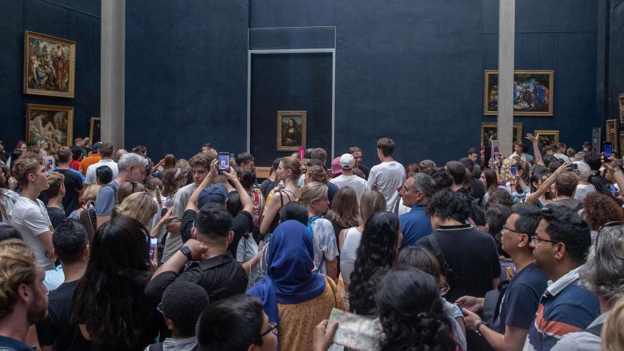 A swarm of visitors take picture of the painting the Mona Lisa in a overcrowded gallery in the Louvre