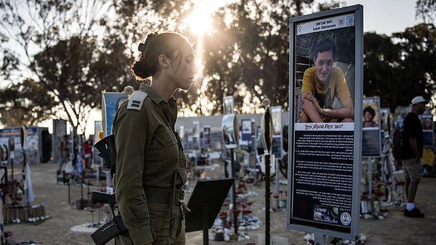 An Israeli army soldier stands before the memorial of a victim of the 2023 October 7 attacks at the Nova Festival grounds