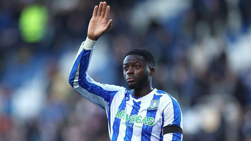 Dominic Iorfa in the blue and white striped shirt of Sheffield Wednesday waves to the crowd.