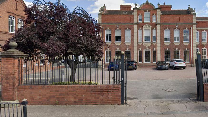 Outside the main entrance of RGS School in Worcester, where large gates are open into a courtyard where cars are parked