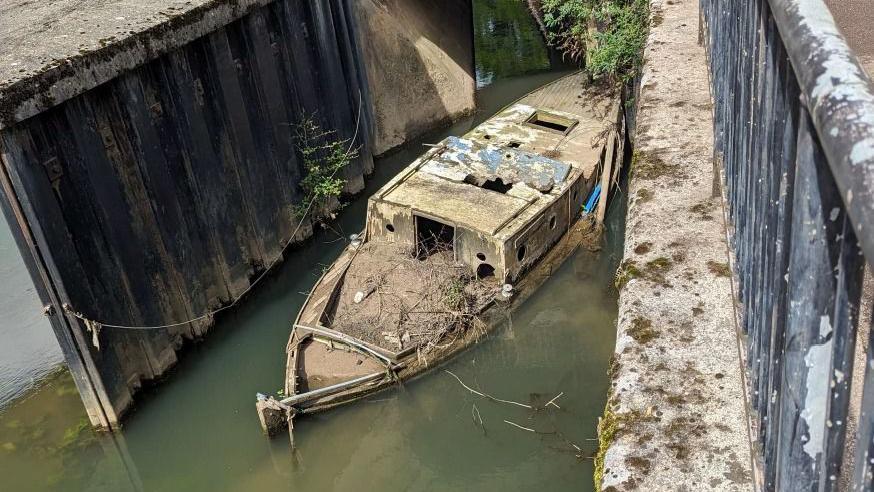 A sunken boat in the river in Bath. It has disintegrated and is blocking the waterway. Debris can be seen on it's roof, which has holes in it.