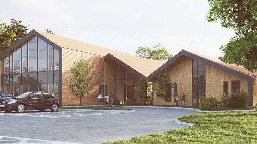 A CGI image of a modern red-brick and glass front building with sloping rooves, viewed across a car park in the sunshine