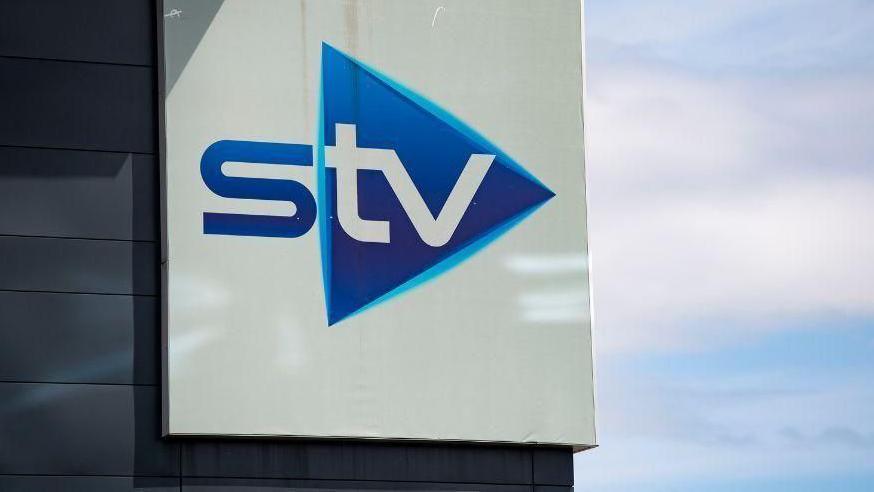 Close up of a blue and white STV sign on a building, photographed against a cloudy blue sky