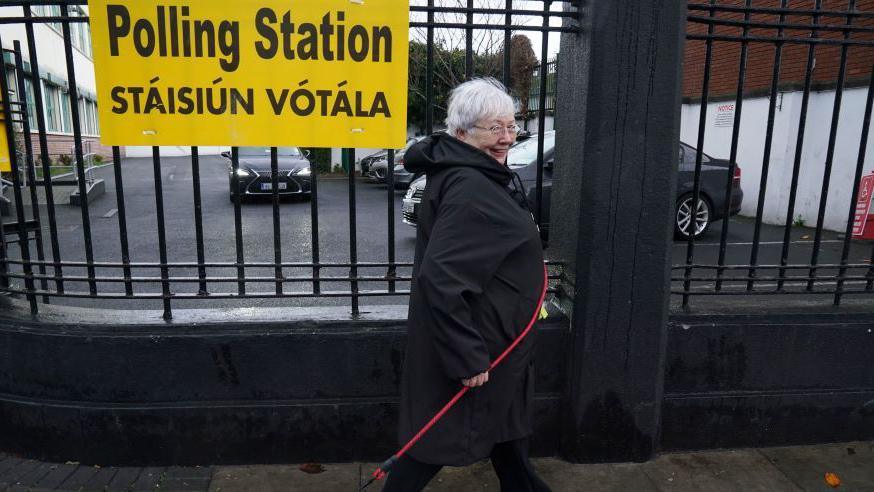 A woman walks with a dog lead outside of a polling station