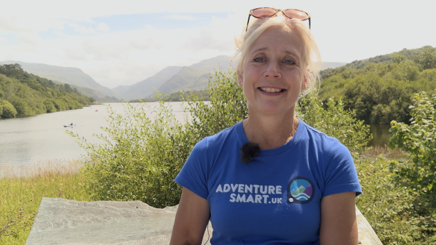 Emma Edwards-Jones, wearing a blue Adventure Smart t-shirt, stood in front of a large lake with Yr Wyddfa in the background