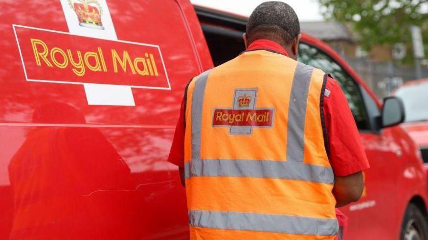 Postal worker stands next to a Royal Mail branded van