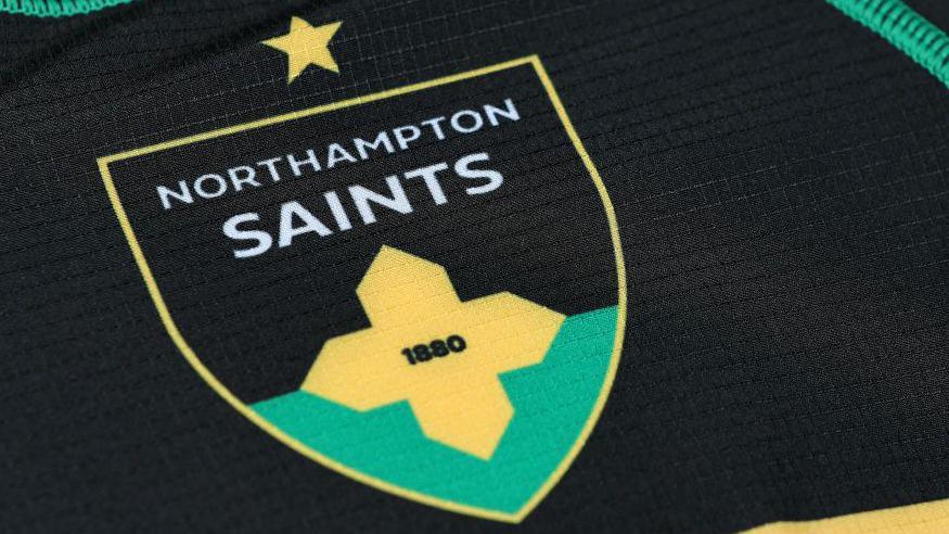 A close-up of a Northampton Saints badge on a home jersey.