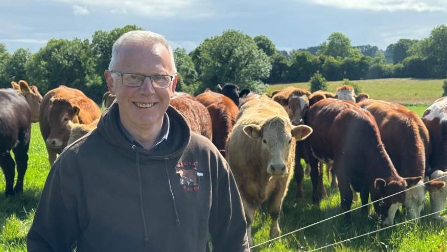 man with glasses standing in front of brown cows