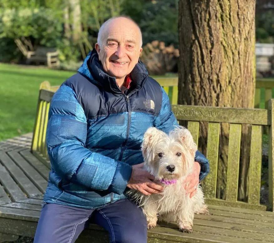 Sir Tony sat on a bench with his white westie Holly Berry. She is wearing a pink collar.