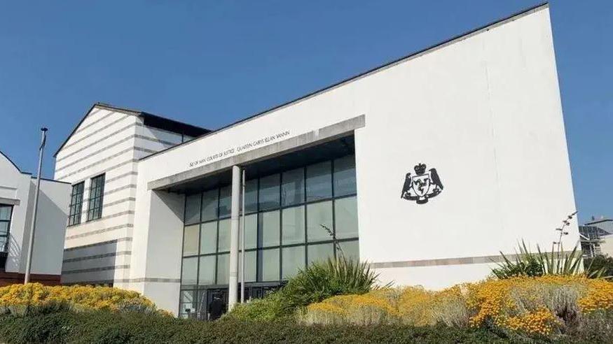 Douglas Courthouse, which is a large white building with a glass fronted entrance and the government crest on the right-hand side.