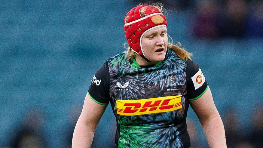 Harlequins' Aoife Wafer wears a red protective head cover during a match 