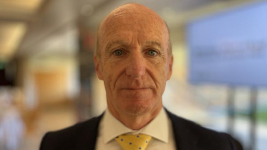 Kevin Keable was in the middle of the image looking towards the camera. He had short grey hair and was wearing a white shirt, with a black suit jacket and yellow tie.