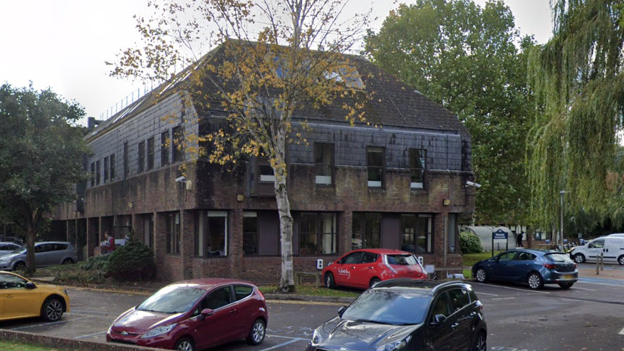 An exterior image of the Waverley Borough Council offices in Godalming. There are a number of cars parked outside the two-storied brown building.