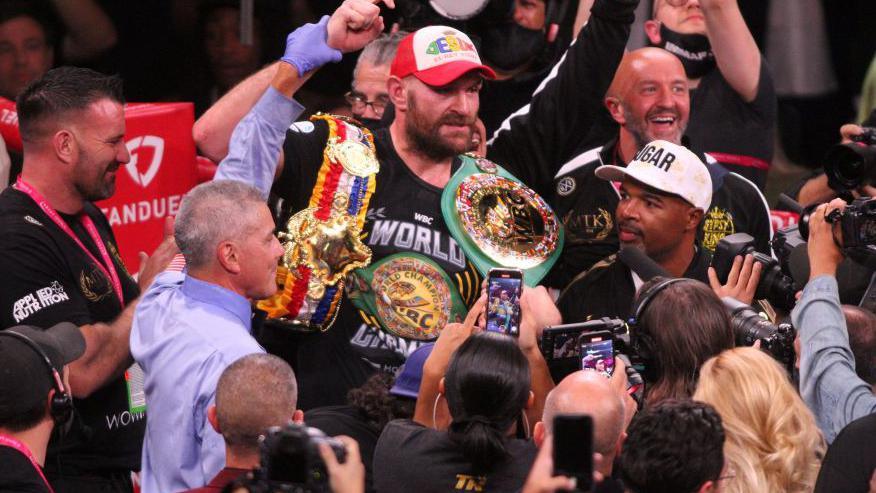 Tyson Fury celebrates surrounded by people in the ring, with his belts around him