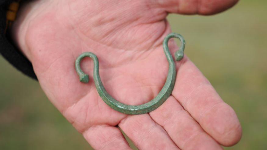 A curved piece of corroded metal with curved ends in the palm of a person's hand