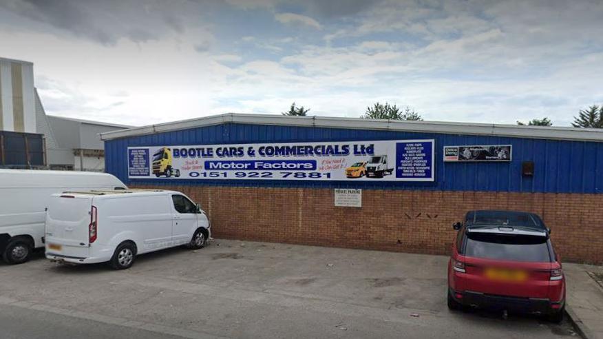 Industrial estate building exterior with blue top and brick bottom - two white vans and a red car are parked outside - a sign reads Bootle Cars & Commecials Ltd 