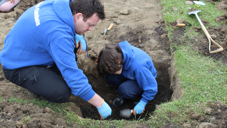 A man crouches down with a young boy who is digging with a small trowel in a small square area of earth 