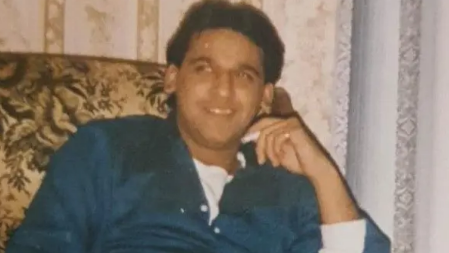 Shami wearing a blue shirt with white buttons and a white top underneath. He is sitting on a patterned arm chair