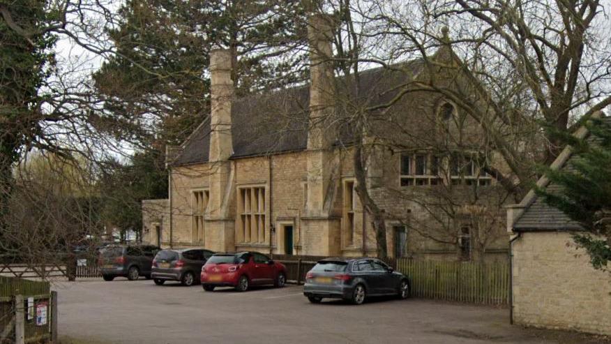 The historic Grade II listed building. It is made of brown bricks and there are four cars parked in front of it