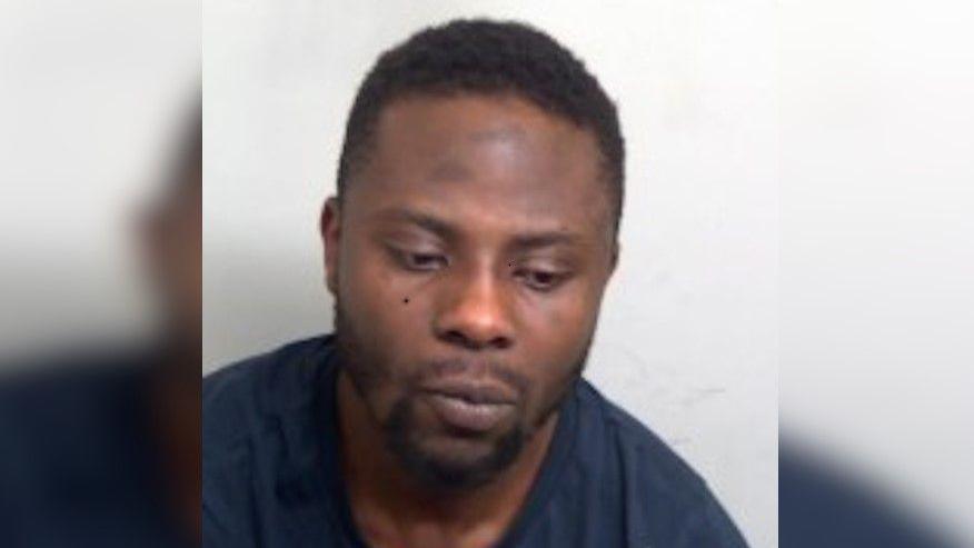 Will Dohmatob is in the middle of the image. He has black short hair and is wearing a navy T-shirt. He is looking toward the floor to the right and sat in front of a white background.
