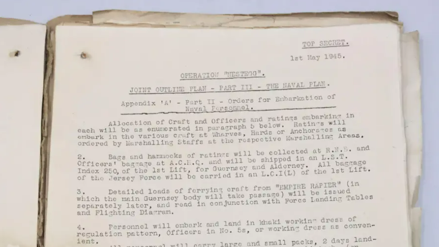An old document in a manila folder. It reads: TOP SECRET. Ist May 1945. OPERATION "NESTEGG". JOINT OUTLINE PLAN - PART ITI - THE NAVAL PLAN Appendix 'A' - Part II - Orders for Enbarkation of - Naval Personnel. Allocation of Craft and Officers and ratings embarking in each will be as enumerated in paragraph 5 below. Ratings will embark in the various craft at Wharves, Hards or Anchorages as ordered by Marshalling Staffs at the rospoctive Marshalling Areas. Bags and harmocks of ratings will be collected at R.N.5. and Officers' bagrage at A.C.F.C. and will be shipped in an L.S.T. Index 250, of the lst Lift, for Guernsey and Alderney. All bagrage of the Jersey Force will be carried in an L.C.I (L) of the lst Lift. Detailed loads of forrying craft from "EMPIRE RAPIER" (in which the main Guernsey body will take passage) will be issued separately later, and read in conjunction with Force Landing Tables and Flighting Diarram. 4. Personnel will embark and land in khaki working dress of regulation pattern, Officers in No. 5s, or working dress as convenient. All personnel will carry largo and small packs, 2 days landing rations, water bottle (filled to capacity), mackintosh, (or oilskin), ground sheet and Army type blanket.