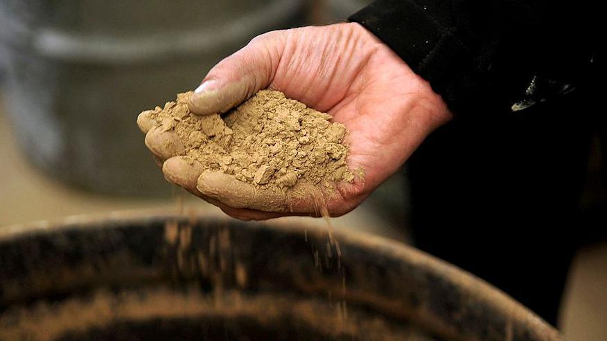 A hand holding light brown soil containing rare earths with some of the soil being allowed to fall though the fingers
