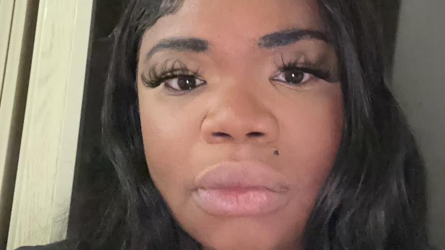 Stacey Llewellyn poses for the camera. She is a young black woman with long hair and false eyelashes.