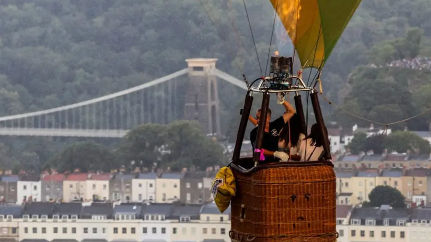 A close-up in the sky of people travelling in a hot air balloon with the Clifton Suspension Bridge in the background