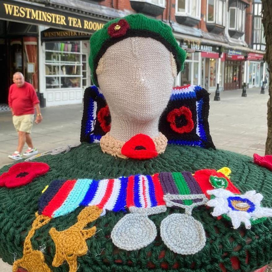 A crochet model of a mannequin wearing a beret surrounded by medals won by Harry Howorth