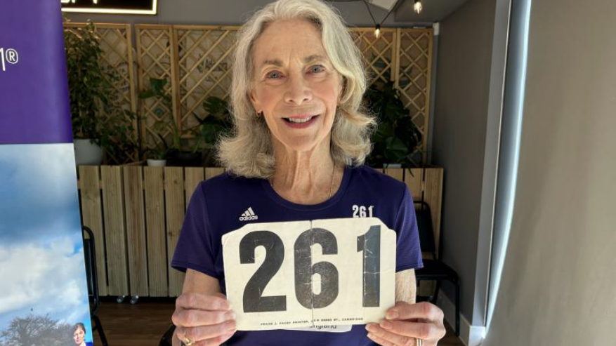 Kathrine Switzer holding her old 261 number and smiling at the camera at the conference.