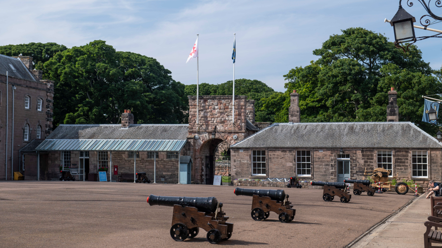 Berwick parade ground, part of Berwick barracks with a row of field guns in the foreground and a low one story building behind them with an archway