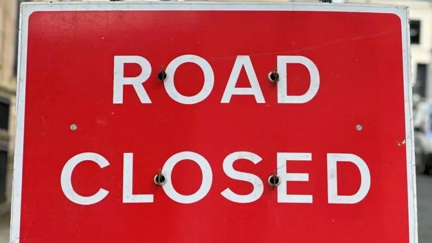 A close up of a large red sign that reads Road Closed.