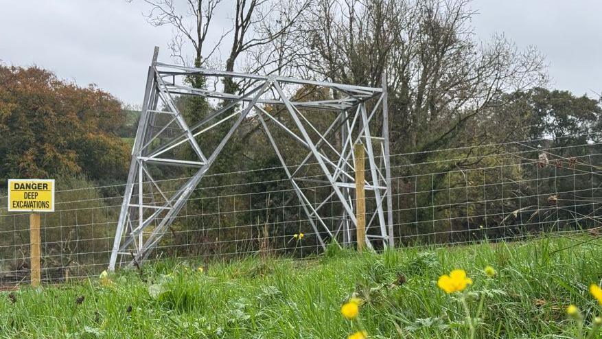 A half built electrical pylon next to a sign which reads 'danger deep excavations