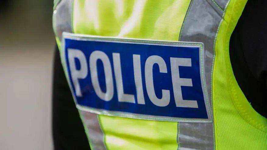 The back a high-vis police jacket with the word POLCIE written in white on a dark blue background