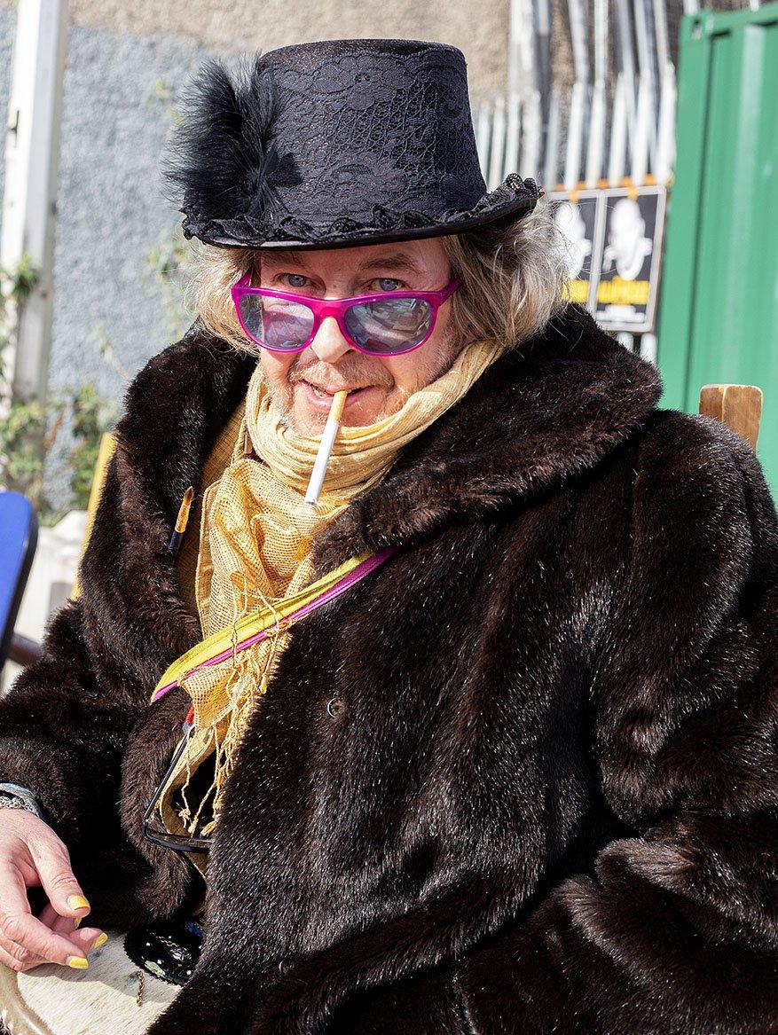 A man wearing pink glasses and a feathered hat