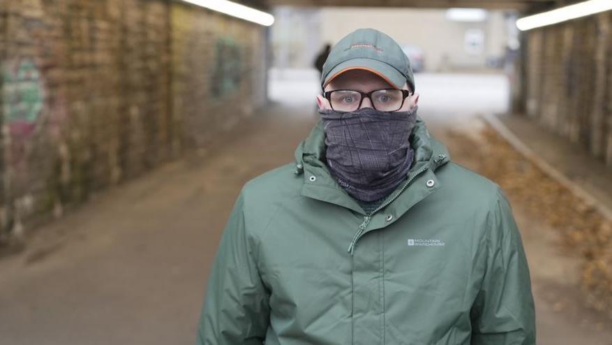 A man wearing glasses, a hat and a coat stares at the camera