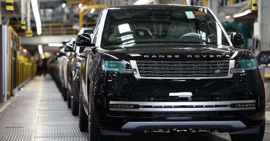 A black Range Rover is at the front of a factory production line that has a metal walkway running alongside the vehicles that are in a queue on the right of the picture.