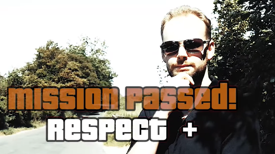 In the middle of the image we can see the words 'mission passed! Respect +' - in the Grand Theft Auto font. Behind that we can a man where a black, short-sleeve shirt with his right hand stroking his chin. He's wearing sunglasses.