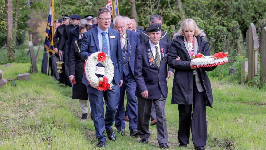 Veteran Ken Cooke leads a procession through the graveyard