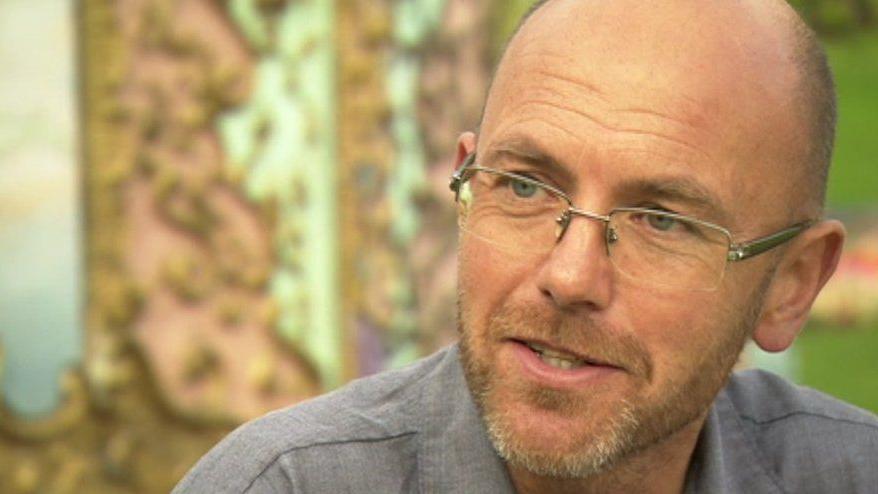 Close up of Wayne Hemingway in front of an elaborately carved gold and green structure