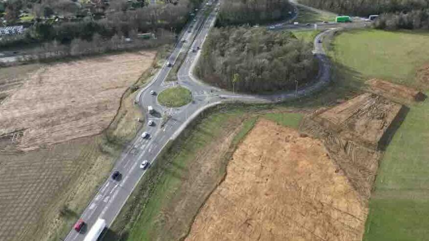 Aerial picture of the excavation site with earth removed, next to a roundabout and a small area of trees next to the road. The A47 goes over the A1 in the background