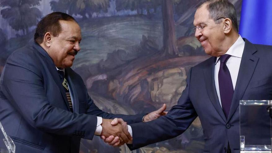 Russian Foreign Minister Sergei Lavrov (R) shakes hands with his Sudanese counterpart Ali Youssef Ahmed Al-Sharif during a press conference. Both men are wearing suits and are standing in front of a large oil painting.