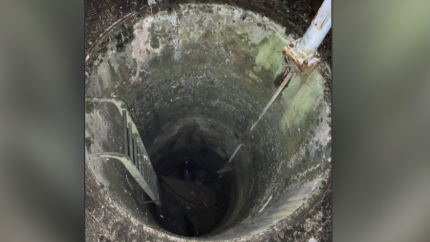 Image of deep round tank with metal ladder visible on one side going down into the tank and a pipe on the other side.