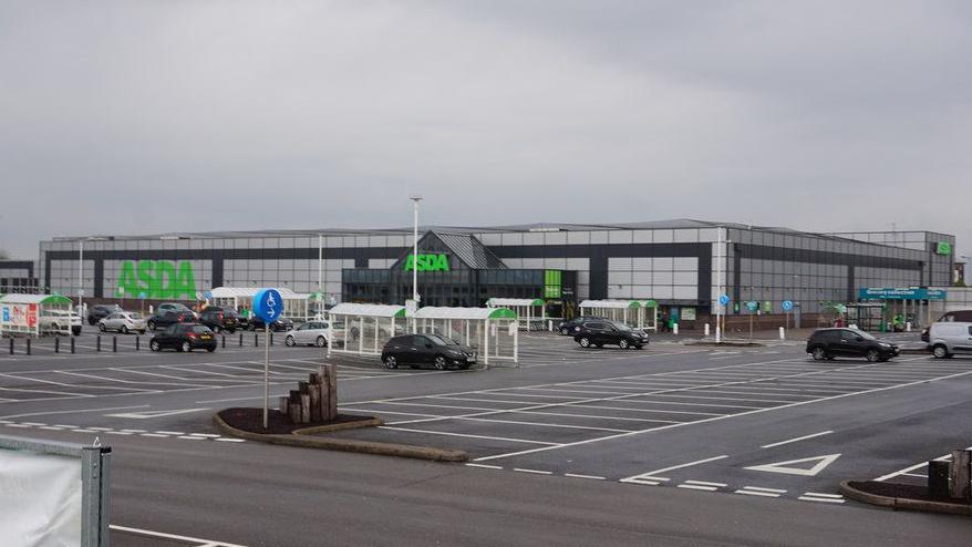 The outside of an Asda supermarket with a car park with with a few cars parked in bays 