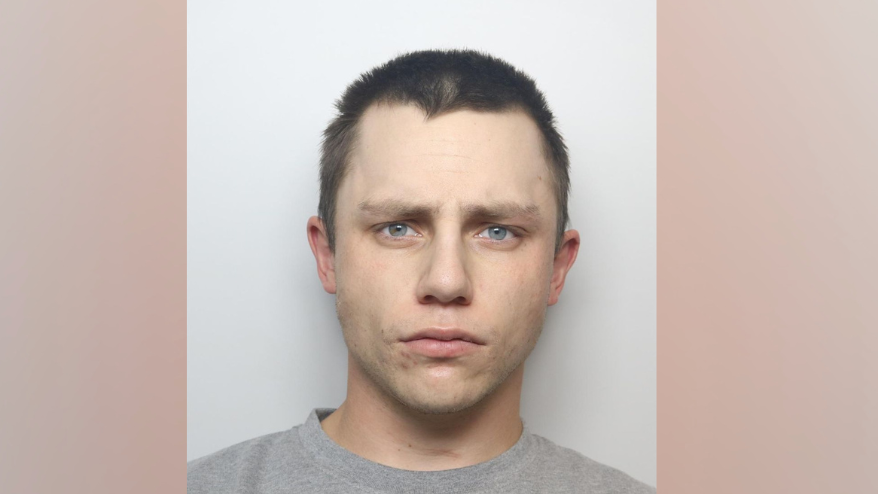 George Wild is wearing a grey sweatshirt and is looking directly at the camera. He has short dark hair and is clean shaven