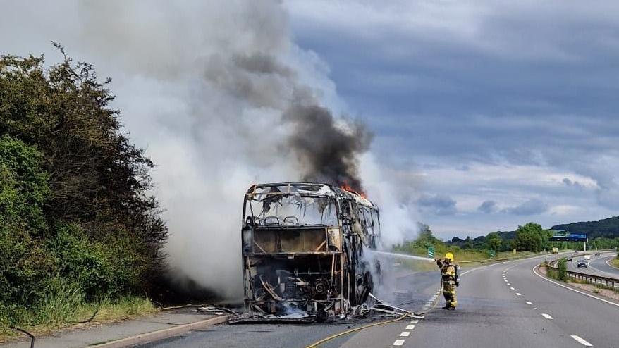 Firefighter pointing water house at bus gutted by fire